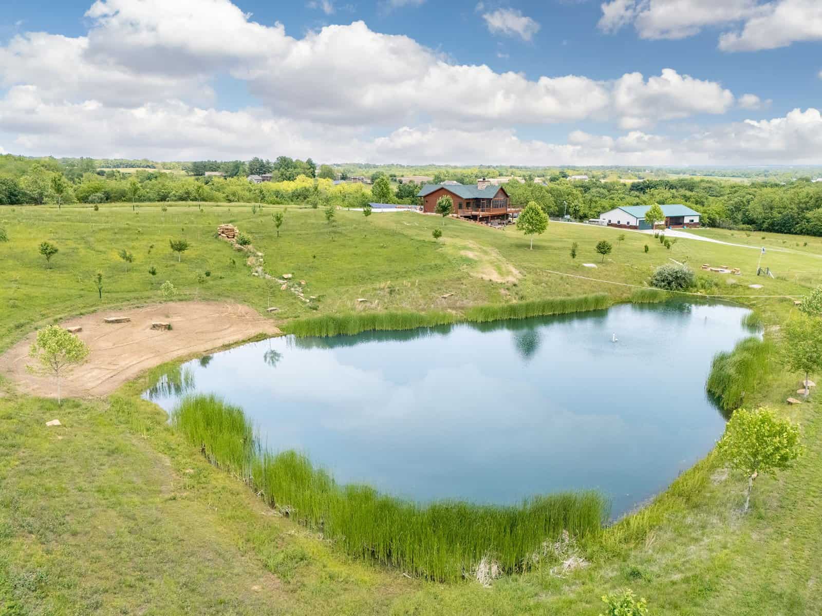 The stocked pond at Selah Hills Ranch, with the lodge and guest building on the ridge above the pasture.