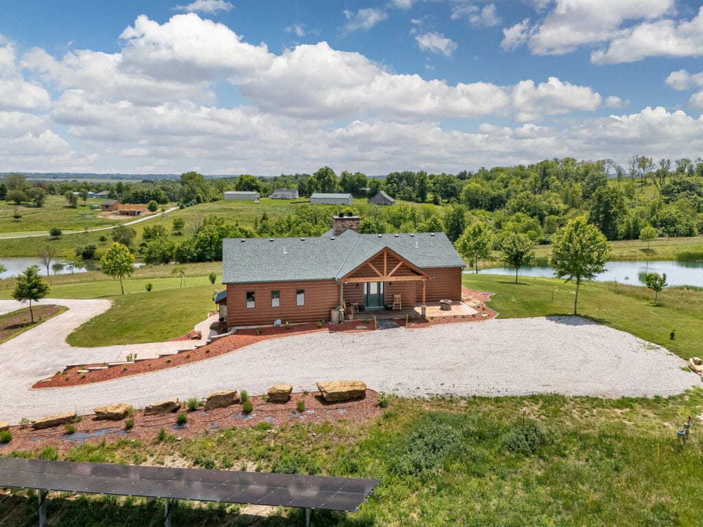 Aerial view of Selah Hills Ranch showing the guest lodge, a pond on each side, the gravel drive lined with limestone boulders, and the solar array in the foreground.