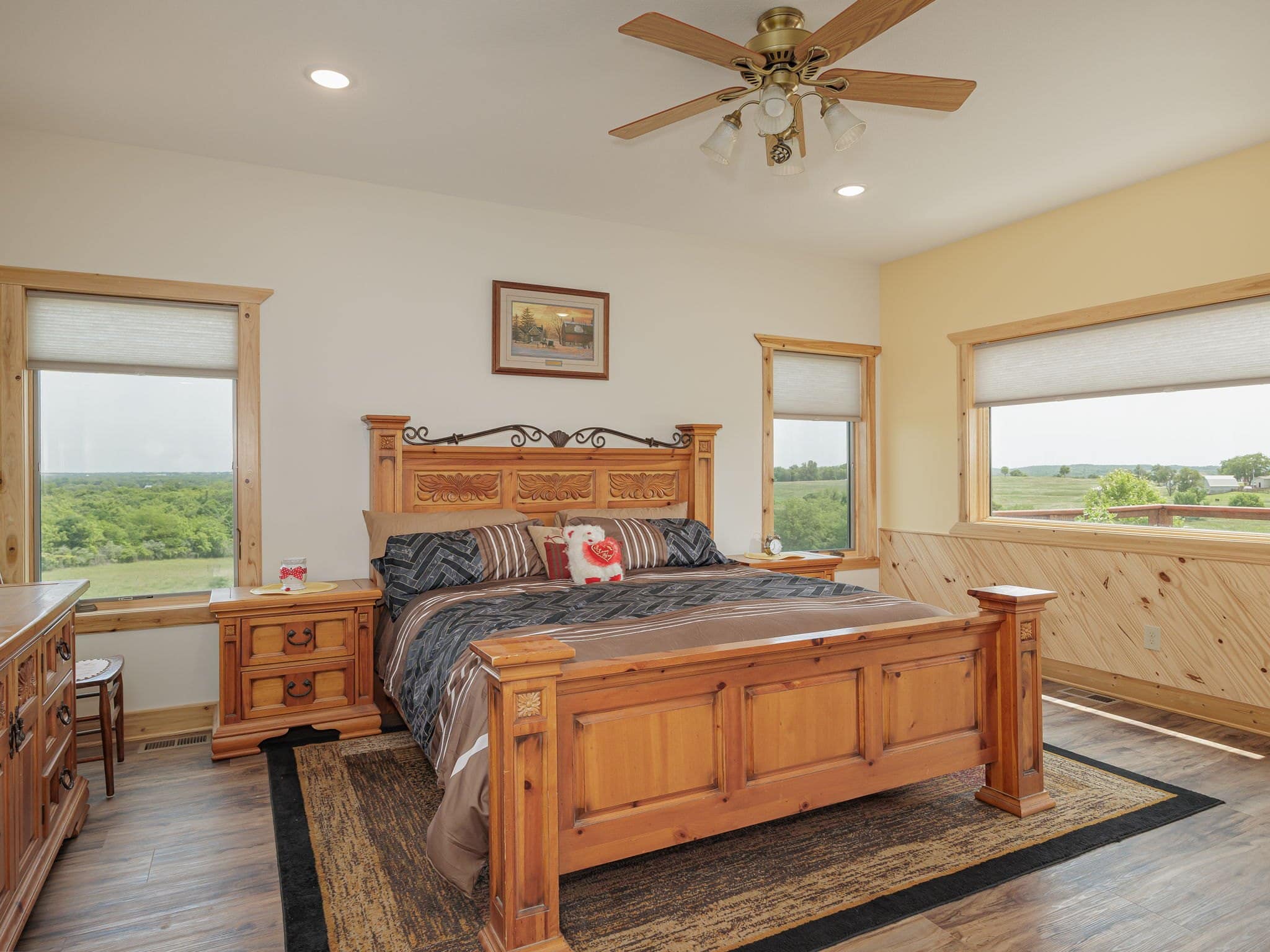 A guest bedroom at Selah Hills Ranch with a tall carved wooden bed between two windows looking over the pasture.