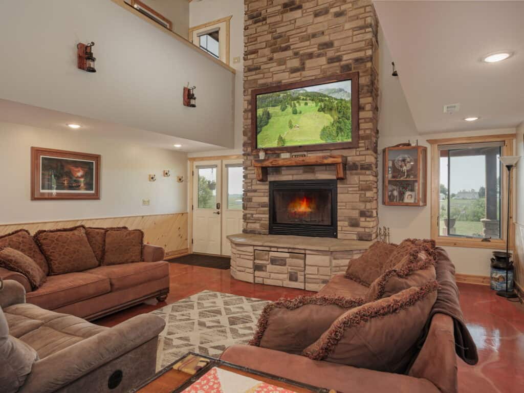 The great room at Selah Hills Ranch with the floor-to-ceiling stone fireplace lit, a vaulted ceiling and deep sofas around a rug.