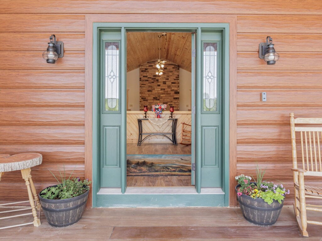 The guest entry at Selah Hills Ranch, a green front door standing open beside rocking chairs and whiskey-barrel planters of flowers.