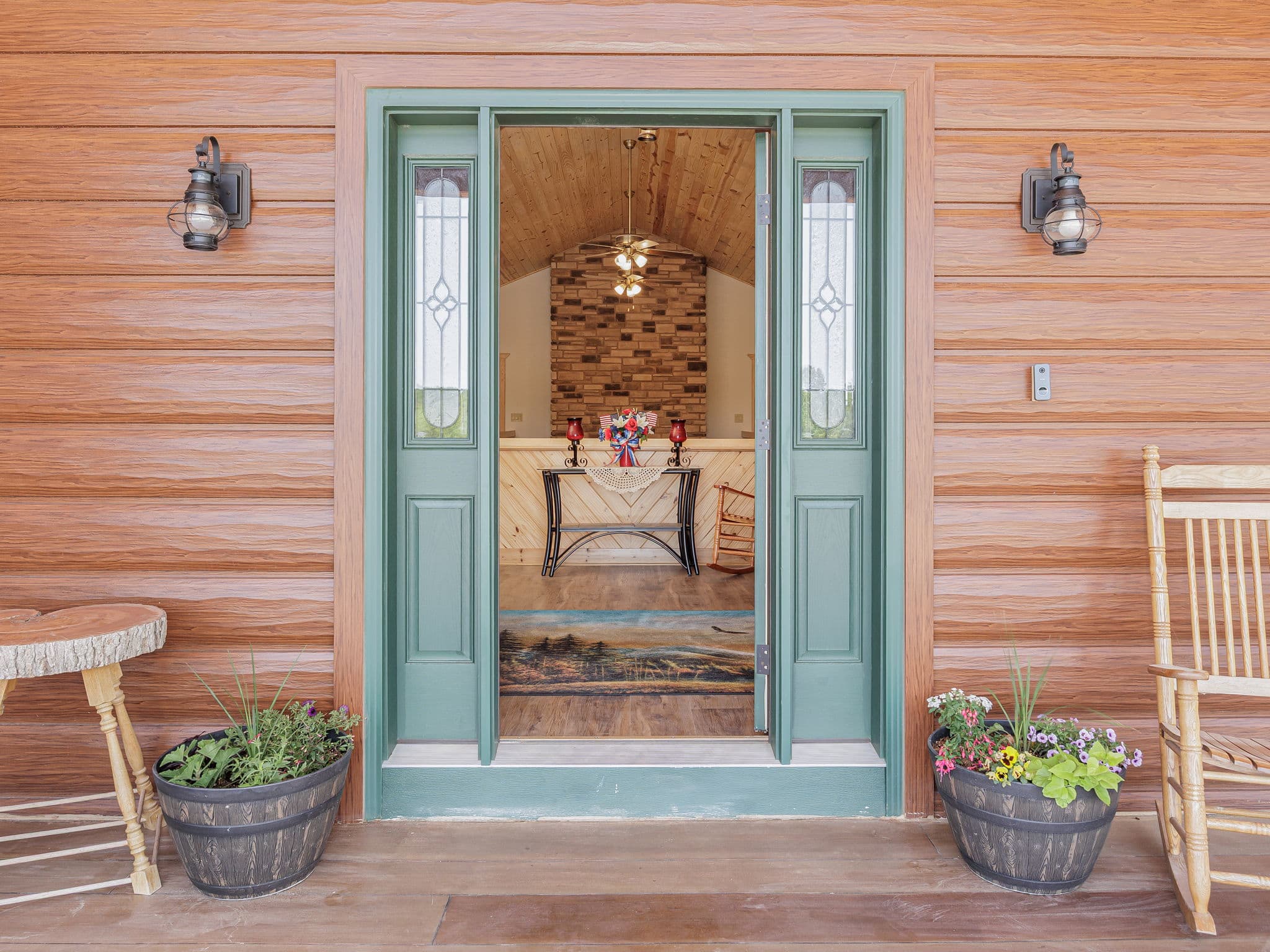 The guest entry at Selah Hills Ranch, a green front door standing open beside rocking chairs and whiskey-barrel planters of flowers.