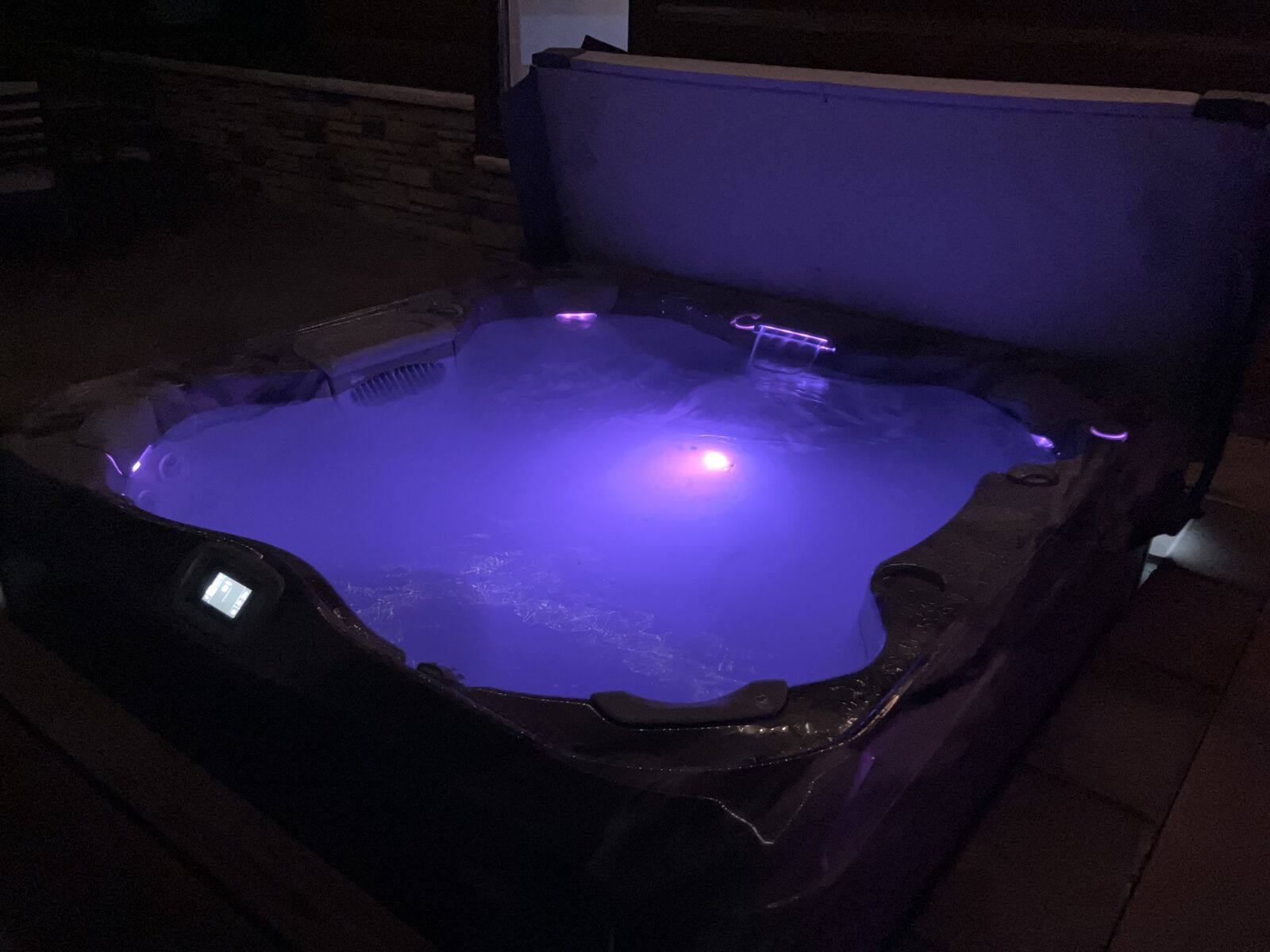 The eight-person hot tub on the covered patio at Selah Hills Ranch at night, lit from within, the water glowing purple against the dark.
