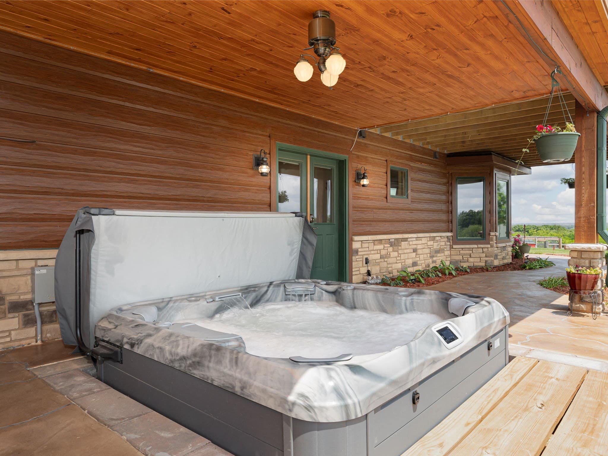 The eight-person hot tub on the covered stone patio beneath the deck at Selah Hills Ranch, looking out over the pasture.