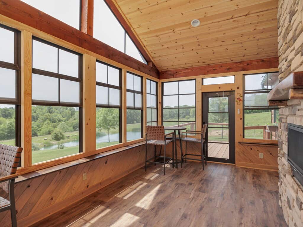 The sun room at Selah Hills Ranch, a timber-framed room with a wall of windows looking out over the stocked pond and pasture.
