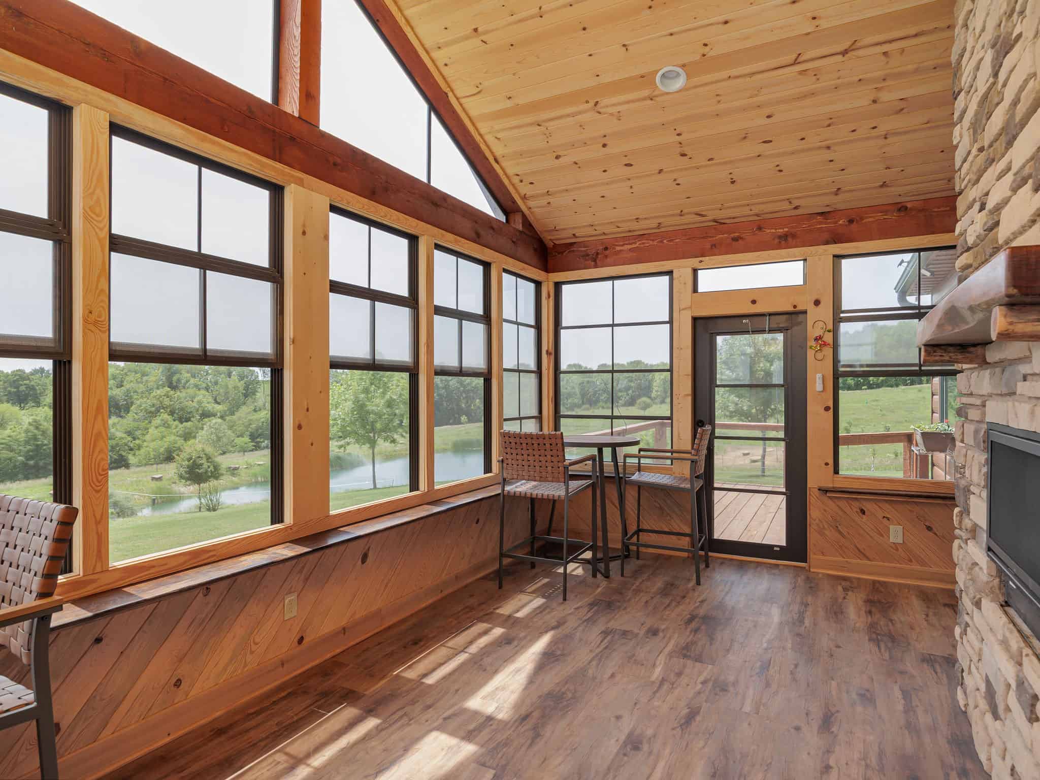 The sun room at Selah Hills Ranch, a timber-framed room with a wall of windows looking out over the stocked pond and pasture.