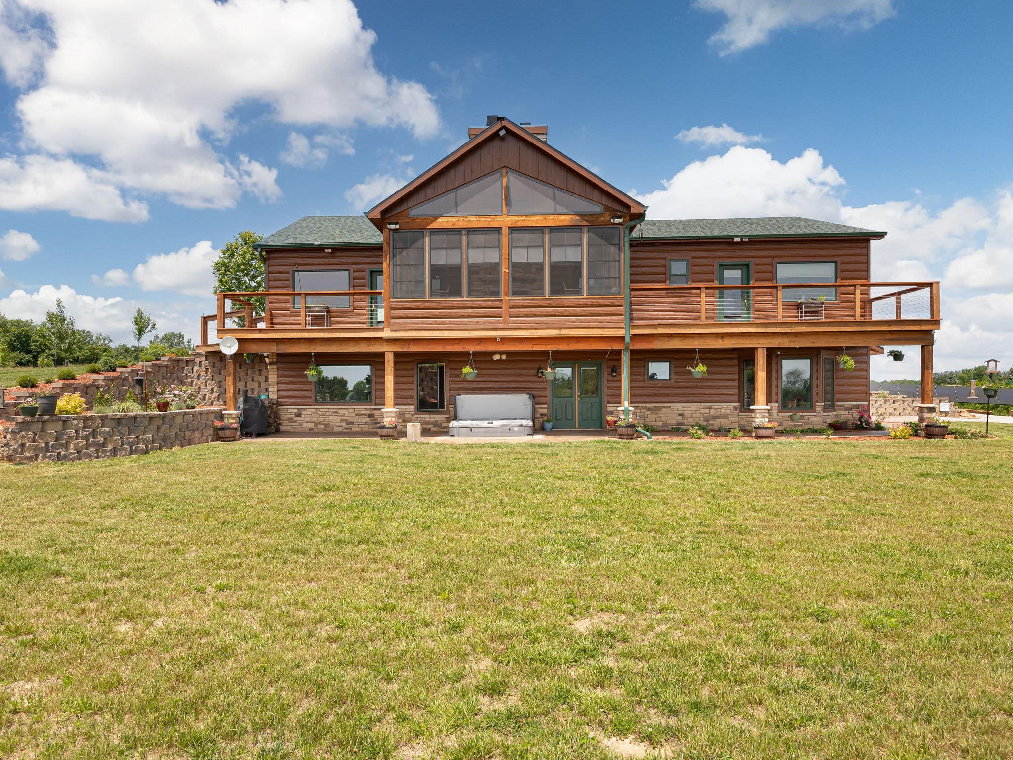 The lodge at Selah Hills Ranch seen from the lawn, a two-storey log home with a screened porch, a full-width deck and a walkout lower level under a green roof.