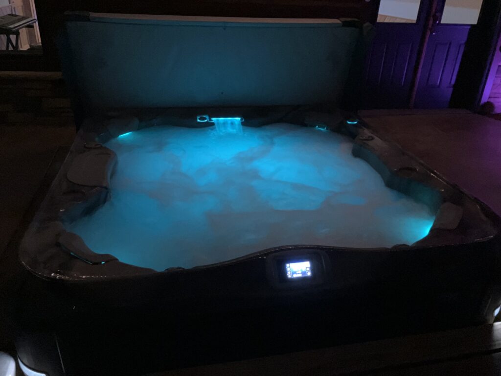 The eight person hot tub at Selah Hills Ranch lit blue at night with steam rising off the water.